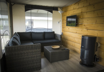 Salottino moderno in una tenda safari Tent Villa al Holiday Park Duinhoeve, con divano e televisione a muro.