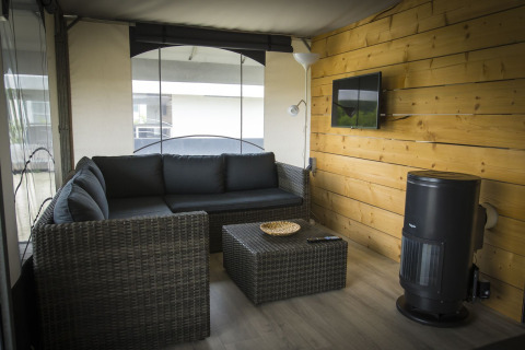 Salottino moderno in una tenda safari Tent Villa al Holiday Park Duinhoeve, con divano e televisione a muro.