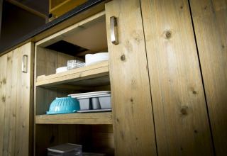 Wooden cabinet with open shelves displaying kitchenware inside a safari tent villa at Holiday Park Duinhoeve.
