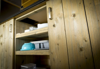 Wooden cabinet with open shelves displaying kitchenware inside a safari tent villa at Holiday Park Duinhoeve.