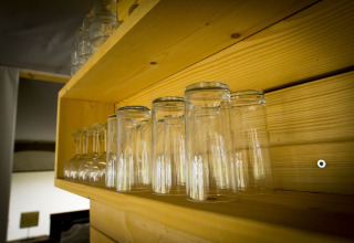 Upside-down glasses on a wooden shelf inside a safari tent at Holiday Park Duinhoeve, Netherlands.