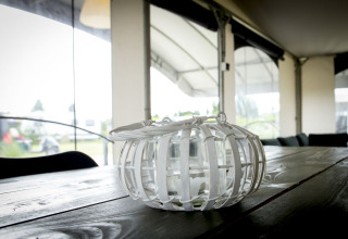 Photo intérieure d'une lanterne en verre à cadre blanc sur une table en bois dans une tente safari au Holiday Park Duinhoeve.