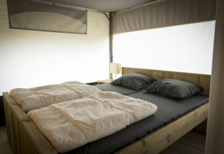 Innenansicht eines bequemen Betts in einem Safarizelt-Tent Villa im Holiday Park Duinhoeve, Niederlande.