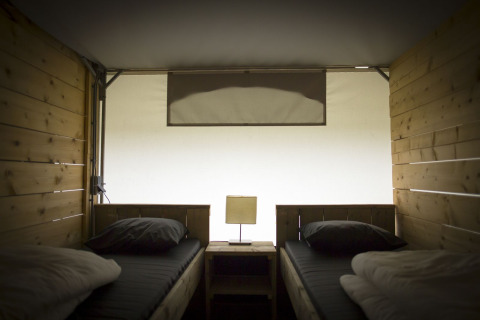 Vista interior de una carpa villa safari con dos camas individuales y paneles de madera en Holiday Park Duinhoeve, Países Bajos.