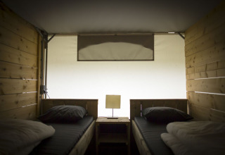 Interior view of a safari tent villa with two single beds and wood paneling at Holiday Park Duinhoeve, Netherlands.