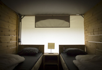 Vista interior de una carpa villa safari con dos camas individuales y paneles de madera en Holiday Park Duinhoeve, Países Bajos.