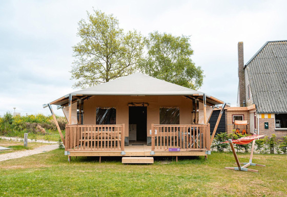 Safaritent Villatent Cottage in Vakantiepark De Nollen, Nederland, met veranda en hangmat aan de voorkant.