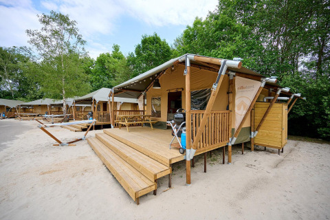 Safari tent Villatent Cottage at Vakantiepark Sallandshoeve in the Netherlands with a wooden deck and trees.