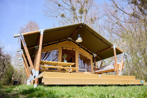 Safari tent Villatent Compact met overdekt houten terras, picknicktafel en zitbank in groene natuur.