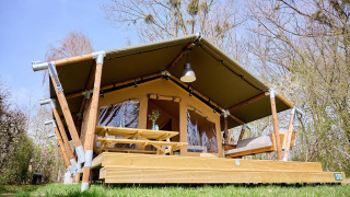 Safari tent Villatent Compact with covered wooden deck, picnic table, and bench in a green setting.