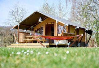 Tenda safari Villatent Compact con veranda in legno, tavolo da picnic e amaca immersa nel verde.