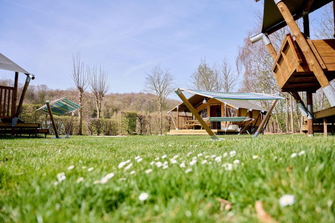 Groene camping met Villatent Compact safaritenten, hangmatten en houten hutten onder een blauwe lucht.
