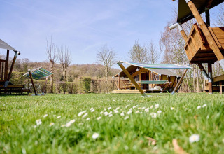 Groene camping met Villatent Compact safaritenten, hangmatten en houten hutten onder een blauwe lucht.