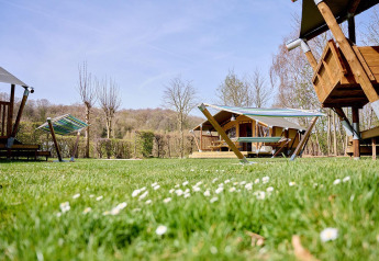Grüner Campingplatz mit Villatent Compact Safarizelten, Hängematten und Holzhütten unter blauem Himmel.