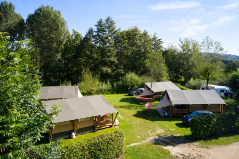 Safari tents Villatent Compact on a grassy campsite surrounded by trees under a bright blue sky.