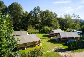 Safari tents Villatent Compact on a grassy campsite surrounded by trees under a bright blue sky.