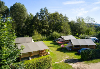 Safari telte Villatent Compact på en grøn campingplads omgivet af træer under en blå himmel.