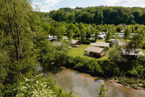 Scenic view of Villatent Compact safari tents by a river, surrounded by lush forest and campsite grounds.