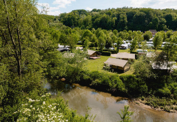 Vista panorámica de tiendas safari Villatent Compact junto a un río, rodeadas de bosque y zona de camping.