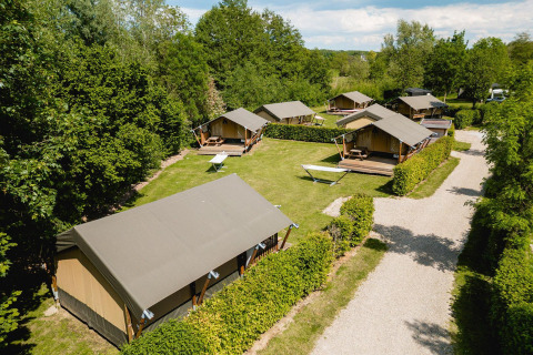 Cinq tentes safari Villatent Compact sur un camping verdoyant avec hamacs et arbres tout autour.