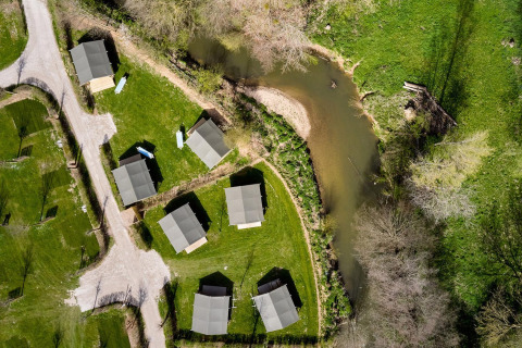 Vista aerea delle tende safari Villatent Compact lungo un fiume, circondate da prato verde e alberi sparsi.