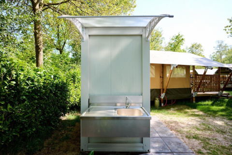 Außen-Spülbecken neben einem Safarizelt im Recreatiepark de Lucht in den Niederlanden, bei sonnigem Wetter.