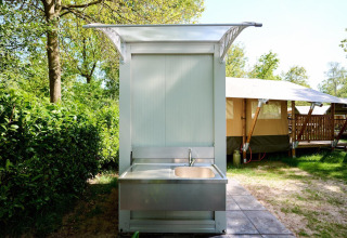 Außen-Spülbecken neben einem Safarizelt im Recreatiepark de Lucht in den Niederlanden, bei sonnigem Wetter.