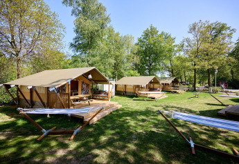 Safaritenten met veranda en hangmatten bij Recreatiepark de Lucht in Nederland, omgeven door bomen.