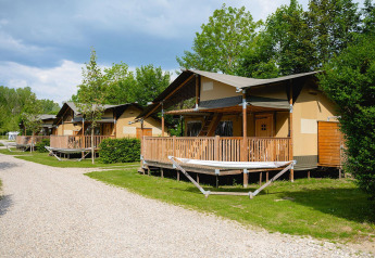 Tiendas safari con terrazas de madera en Camping 't Geuldal en los Países Bajos, rodeadas de árboles.