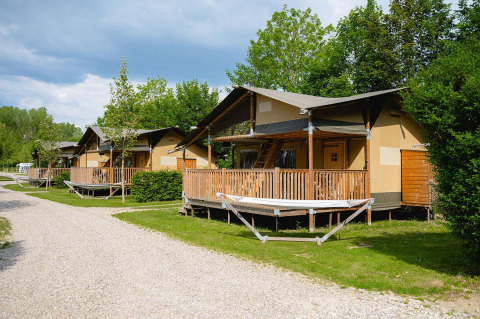 Safari-Zelte mit Holzterrassen auf Camping 't Geuldal in den Niederlanden, umgeben von Bäumen.