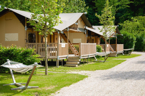 Safaritenten met veranda en hangmat bij Camping 't Geuldal in Nederland, omgeven door groene bomen.