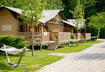 Safari tents with verandas and hammocks at Camping 't Geuldal in the Netherlands, surrounded by trees.