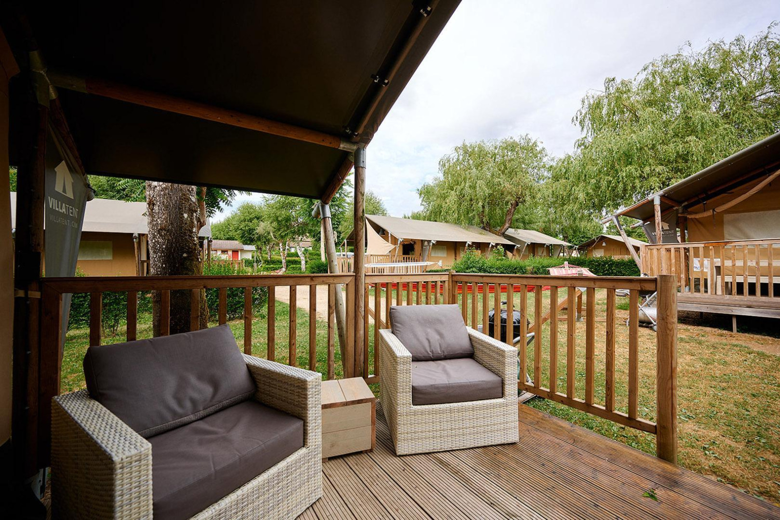 Uitzicht vanaf het terras van een Villatent Nomad bij Camping Le Coin Tranquille in Frankrijk, met stoelen en groen.
