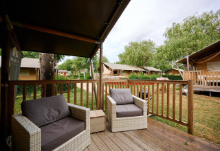 Vista dal terrazzo di una Villatent Nomad al Camping Le Coin Tranquille, Francia, con poltrone e natura verde.