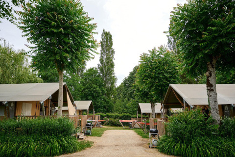 Tiendas safari Villatent Nomad en Camping Le Coin Tranquille, Francia, rodeadas de vegetación y árboles.