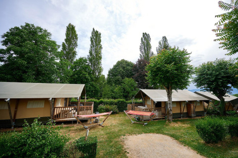 Tiendas safari con terrazas y hamacas en Camping Le Coin Tranquille en Francia, rodeadas de árboles.