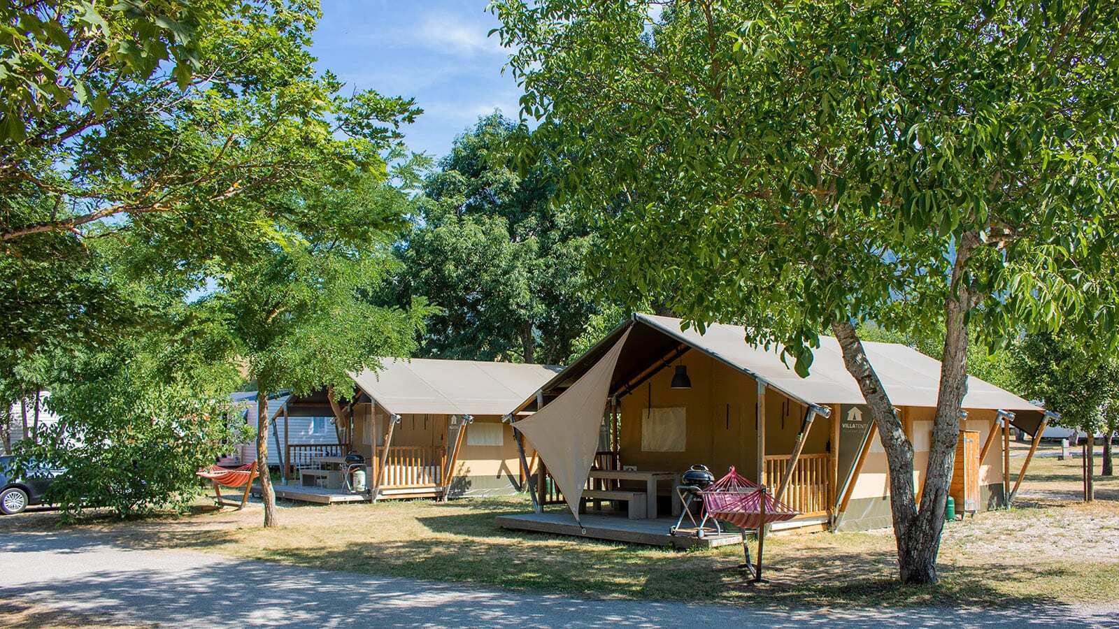 Safaritent Villatent Nomad op Camping Le Lac Bleu in Frankrijk, omgeven door bomen en kampeeruitrusting.
