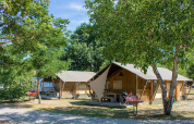 La tienda safari Villatent Nomad en Camping Le Lac Bleu en Francia, rodeada de árboles y equipo de camping.