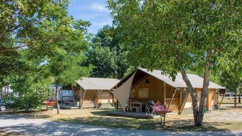 La tienda safari Villatent Nomad en Camping Le Lac Bleu en Francia, rodeada de árboles y equipo de camping.