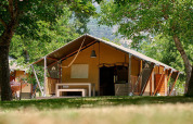 Tienda safari Villatent Nomad en Camping Le Lac Bleu, Francia, rodeada de árboles y vegetación.