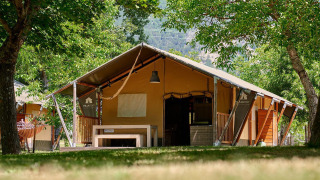 Tienda safari Villatent Nomad en Camping Le Lac Bleu, Francia, rodeada de árboles y vegetación.