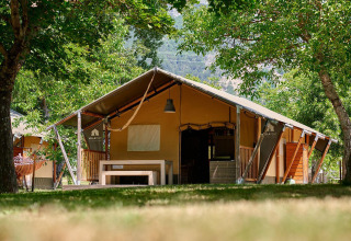 Tienda safari Villatent Nomad en Camping Le Lac Bleu, Francia, rodeada de árboles y vegetación.