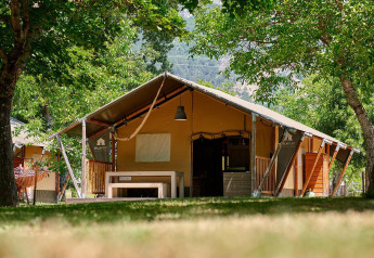 Tienda safari Villatent Nomad en Camping Le Lac Bleu, Francia, rodeada de árboles y vegetación.