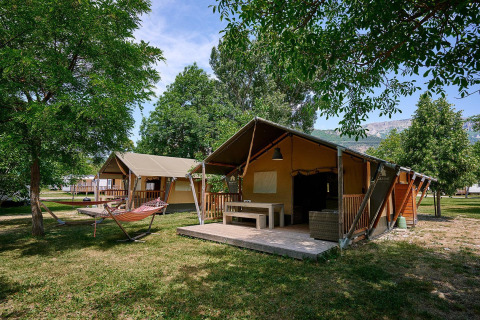 Tiendas safari con terrazas y hamacas en Camping Le Lac Bleu, Francia, rodeadas de árboles y naturaleza.
