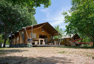 Tienda safari Villatent Nomad en Camping Le Lac Bleu en Francia, rodeada de árboles y muebles de exterior.
