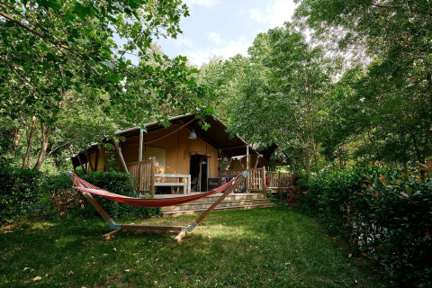 Tienda safari Villatent Nomad en Camping Le Canigou, Francia, rodeada de árboles y una hamaca enfrente.