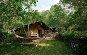 Tienda safari Villatent Nomad en Camping Le Canigou, Francia, rodeada de árboles y una hamaca enfrente.