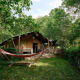 Tienda safari Villatent Nomad en Camping Le Canigou, Francia, rodeada de árboles y una hamaca enfrente.