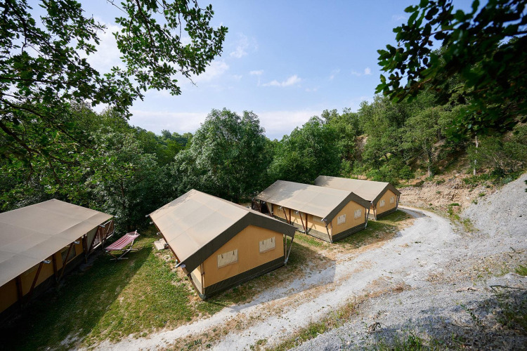 Tiendas safari Villatent Nomad en Camping Le Canigou, Francia, rodeadas de árboles y naturaleza verde frondosa.