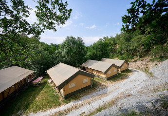 Tiendas safari Villatent Nomad en Camping Le Canigou, Francia, rodeadas de árboles y naturaleza verde frondosa.